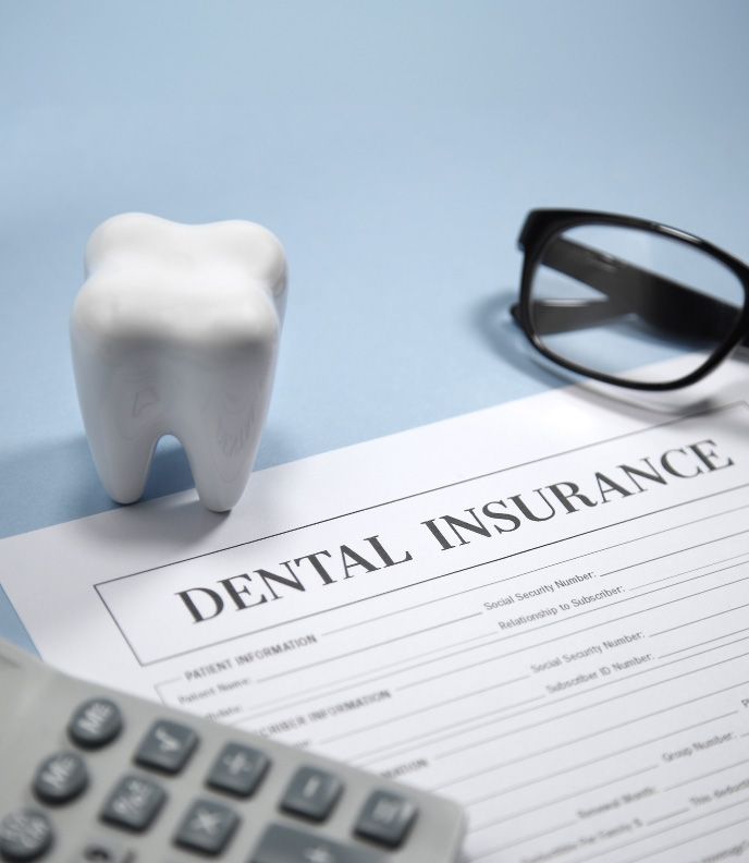 A dental insurance form with patient information, accompanied by a calculator, eyeglasses, and a large model of a tooth | Pleasant Dental