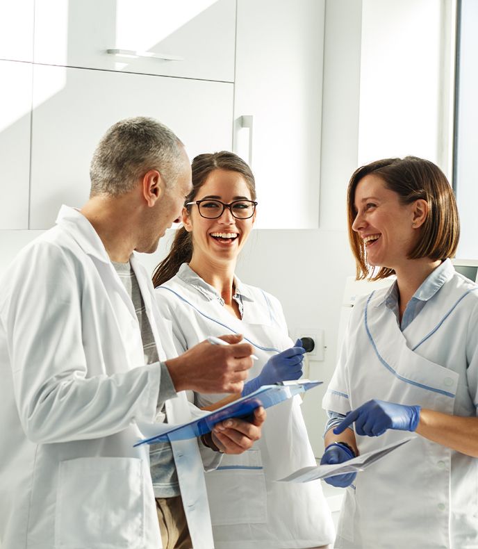 Five smiling office staff members pose in front of a wall with the word "pleasant" displayed prominently. they are dressed in black uniforms | Pleasant Dental